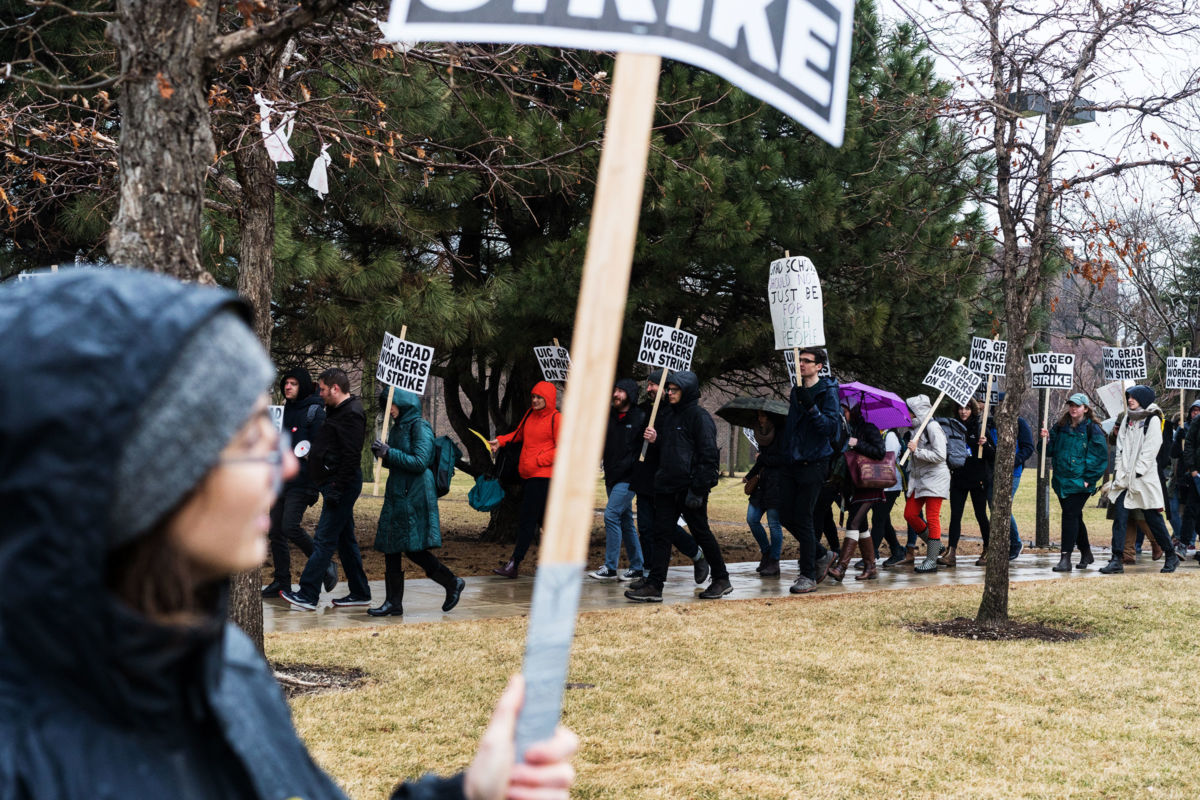 Graduate students march in a line while holding signs declaring them to be on strike