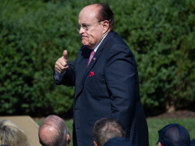 Rudy giuliani makes a thumbs up while walking near reporters