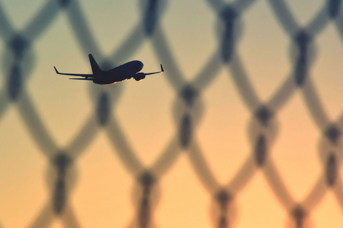 Airplane flying, seen through chainlink fence