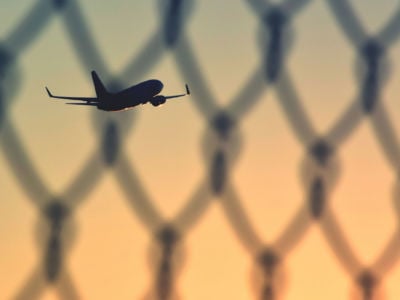 Airplane flying, seen through chainlink fence