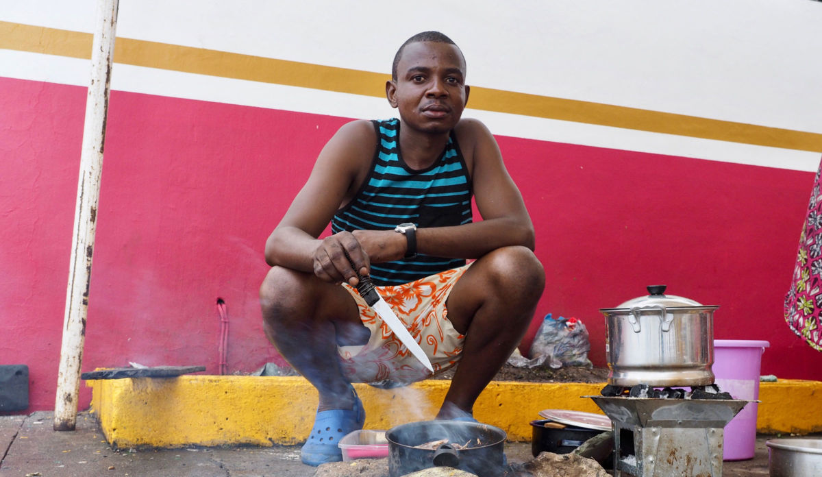 A man squats near a small steaming pot on the ground