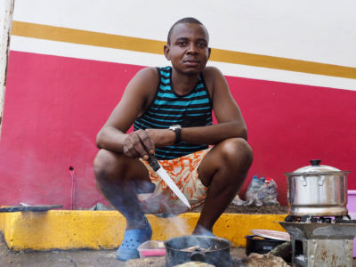 A man squats near a small steaming pot on the ground