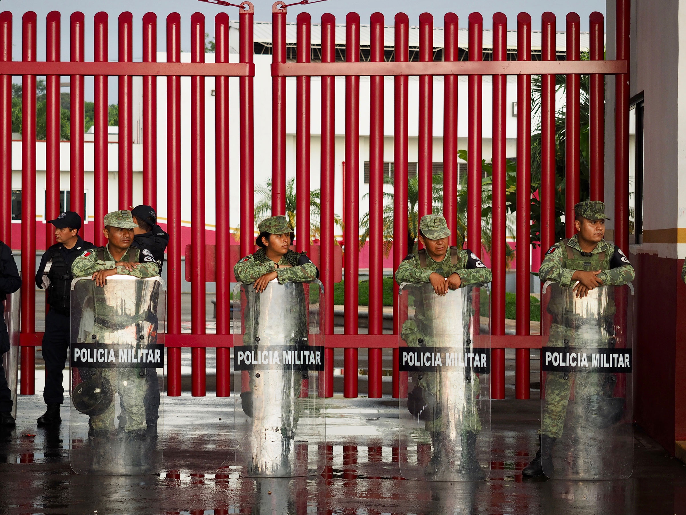 Police with riot shields stand in front of red fencing