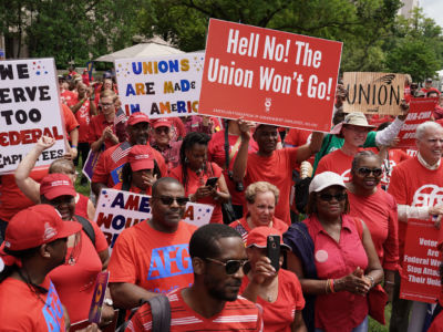Workers wearing red shirts display signs during a protest