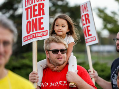 A man protesting man holds a little girl on his shoulders