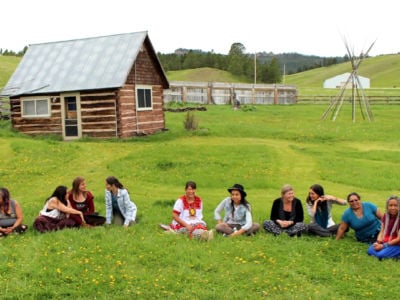 Water protectors of all persuasions gathered in talking circles at Borderland Ranch in Pe’Sla, the heart of the sacred Black Hills, during the first Sovereign Sisters Gathering. At the center are Cheryl Angel in red and white and on her left, Lyla June.