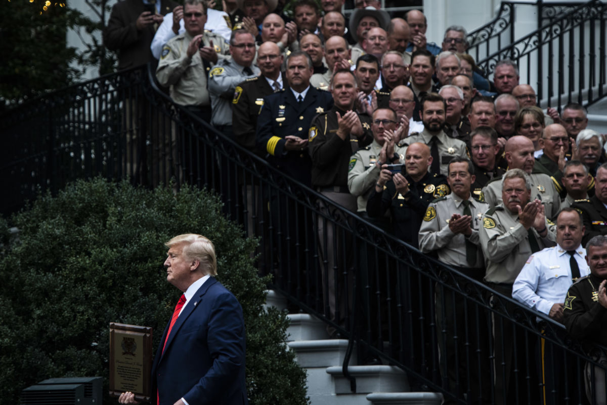 Donald Trump stands near the white house stairs, currently filled with a crowd of clapping sheriffs