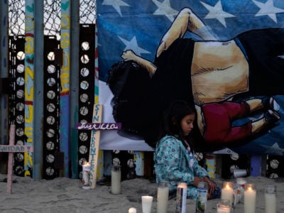 A young girl lights candles in front of a painting of a father holding his dauther