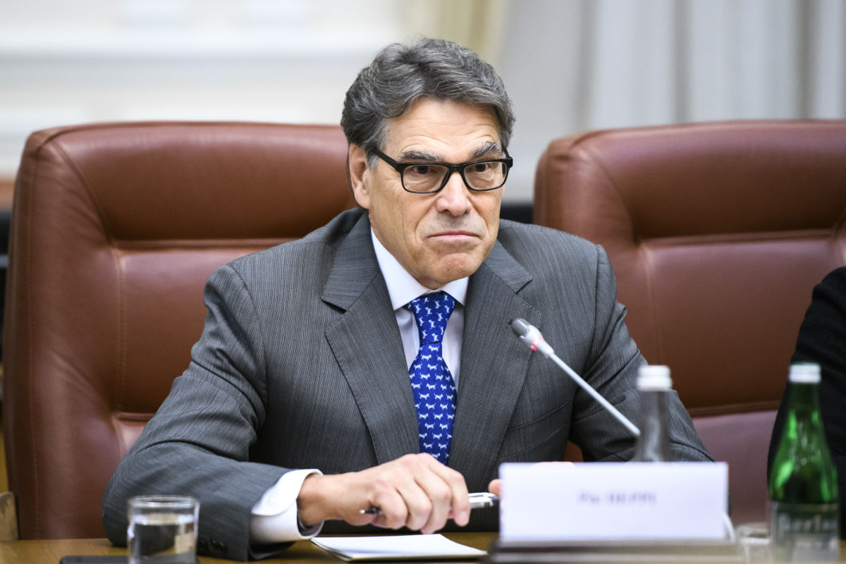 Rick Perry sits at a desk in front of a microphone