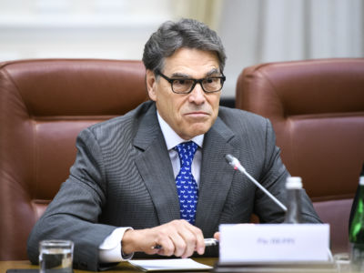 Rick Perry sits at a desk in front of a microphone