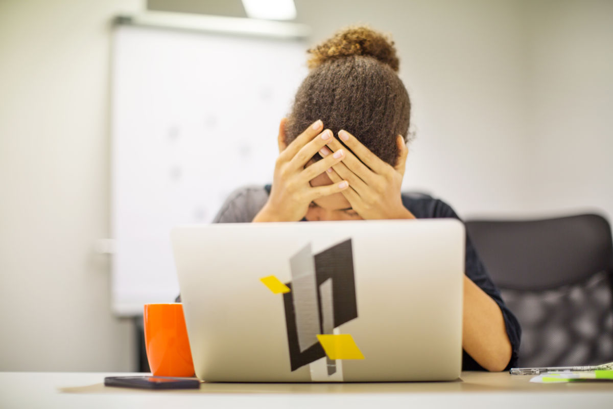 A woman holds her head in her hands in front of her computer screen