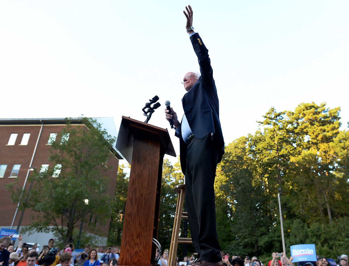 Bernie Sanders raises a hand while standing at a podium during a campaign rally