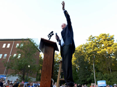 Bernie Sanders raises a hand while standing at a podium during a campaign rally