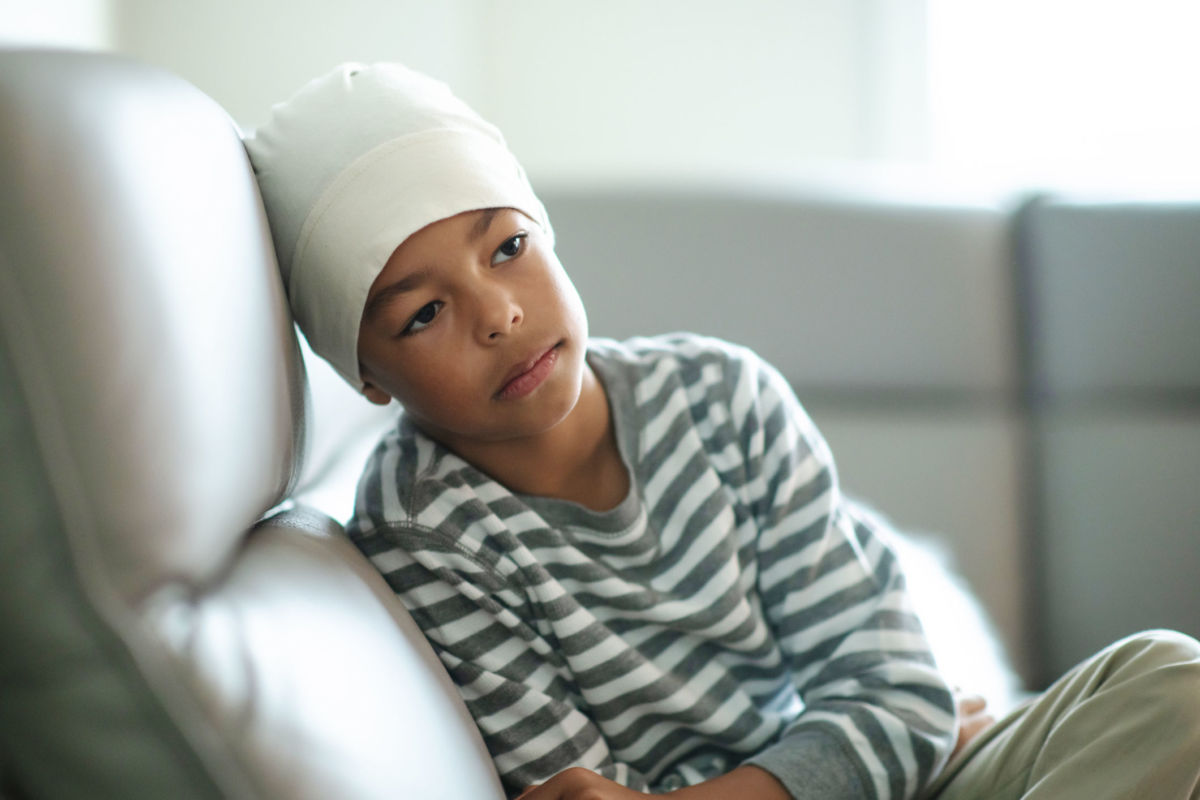 A child wearing a bonnet sadly sits on a couch