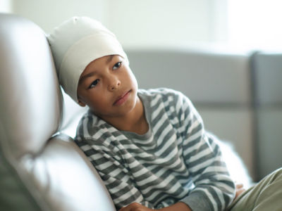 A child wearing a bonnet sadly sits on a couch