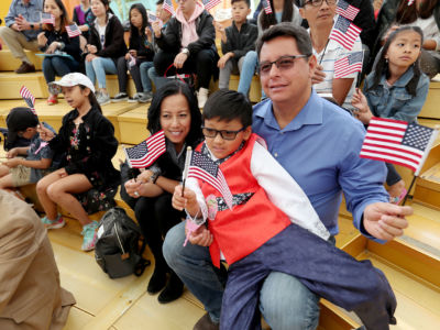 A father sits with his two children, all of whom are waving tiny US flags