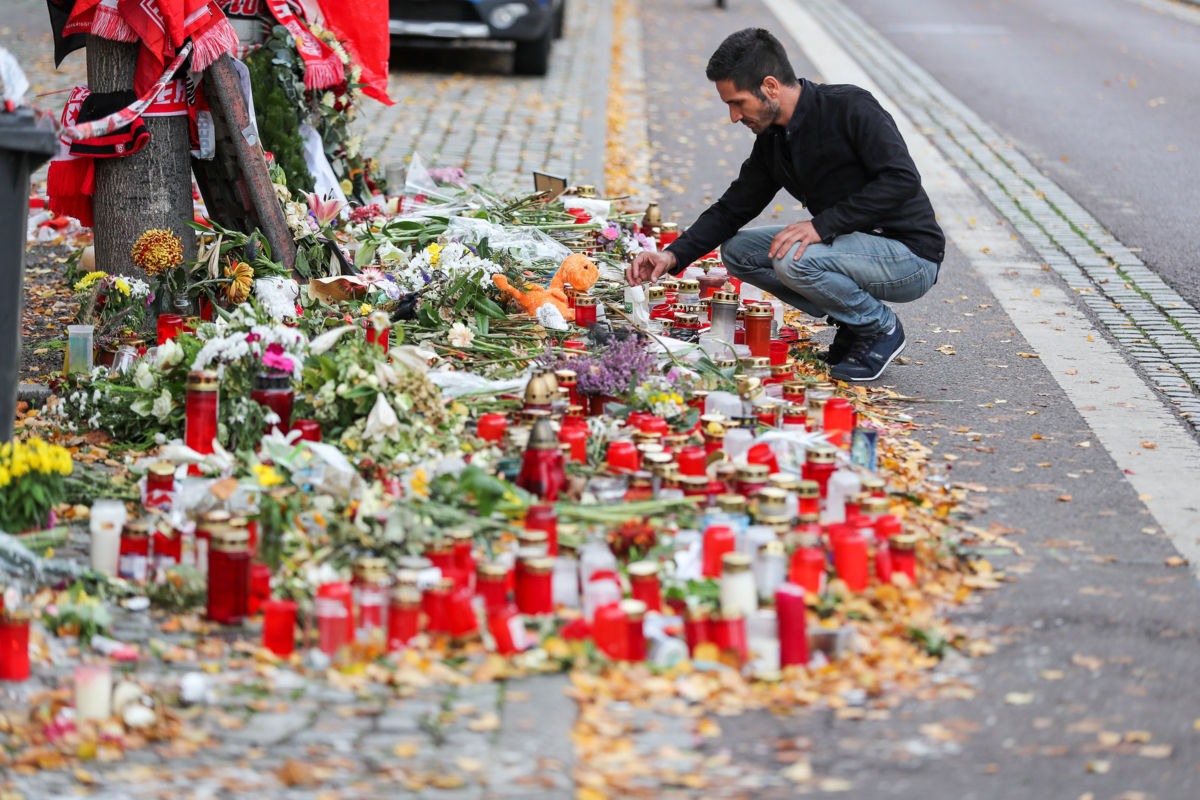 A man kneels by a large memorial of candles and flowers on a city street
