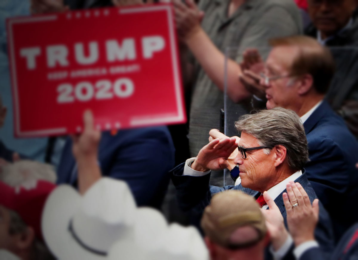 Rick Perry salutes while sitting in the crowd of a Trump Rally