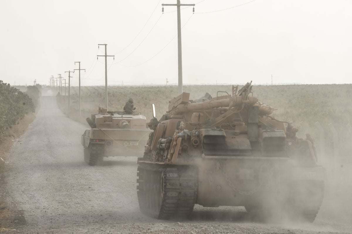 Tanks kick up dust as they drive away down a dirt road