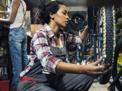 A woman repairs a bike tire while in a shop