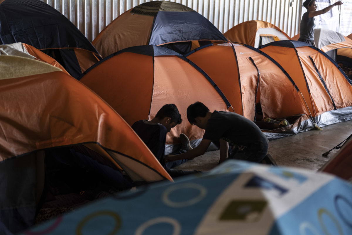 Two children sit on the floor among orange tents in a shelter