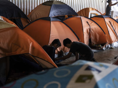 Two children sit on the floor among orange tents in a shelter