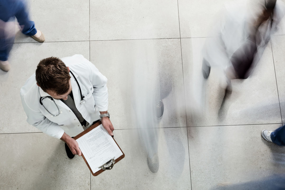 High angle shot of a male doctor looking at a patient's file in a busy hospital