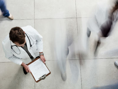 High angle shot of a male doctor looking at a patient's file in a busy hospital