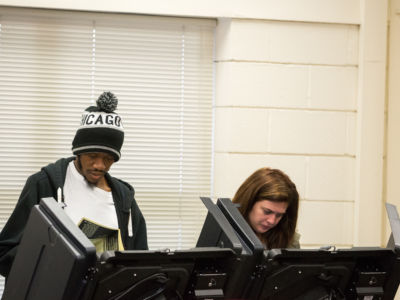 Two people vote next to oneanother at their respective booths