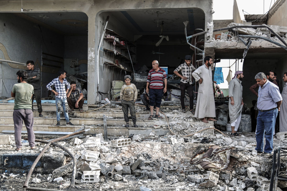 People stand around the piles of grey rubble that used to be buildings