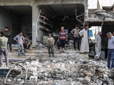 People stand around the piles of grey rubble that used to be buildings