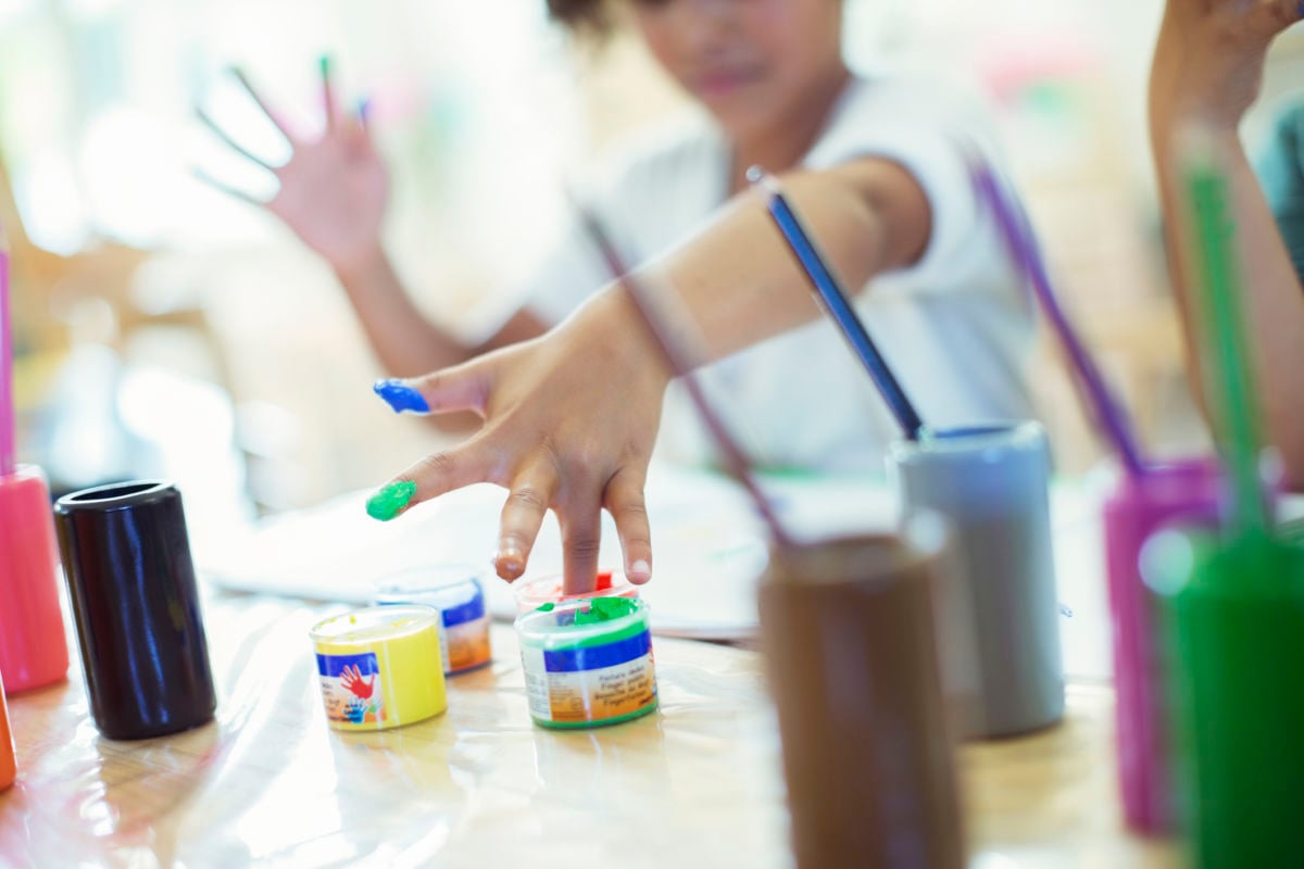 A child dips their fingers into small pots of paint