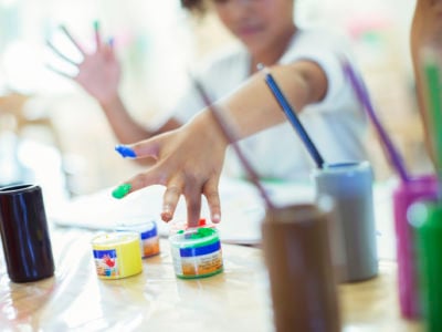 A child dips their fingers into small pots of paint