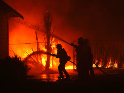 Firefighters hose down a burning house in the midst of a wildfire