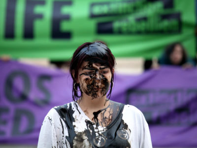 A woman covered in oil stands in front of a green Extinction Rebellion banner