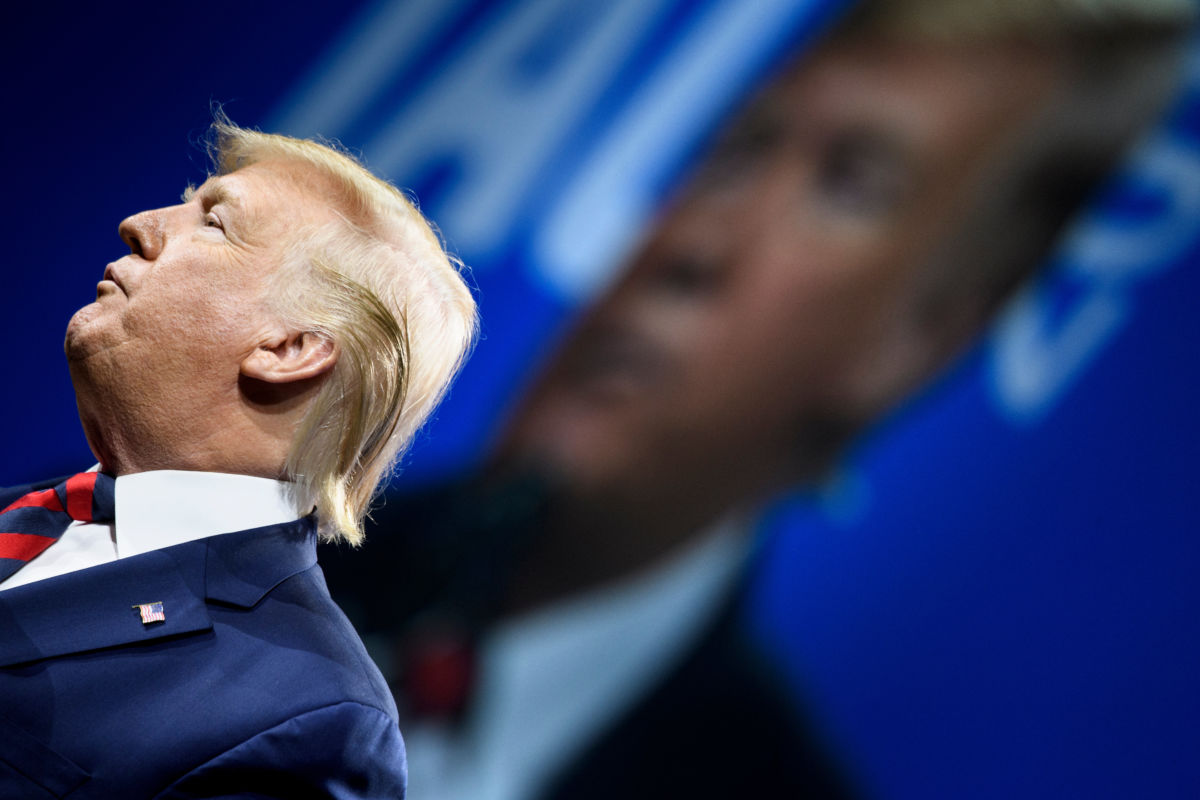 Donald Trump speaks while standing in front of a blue banner