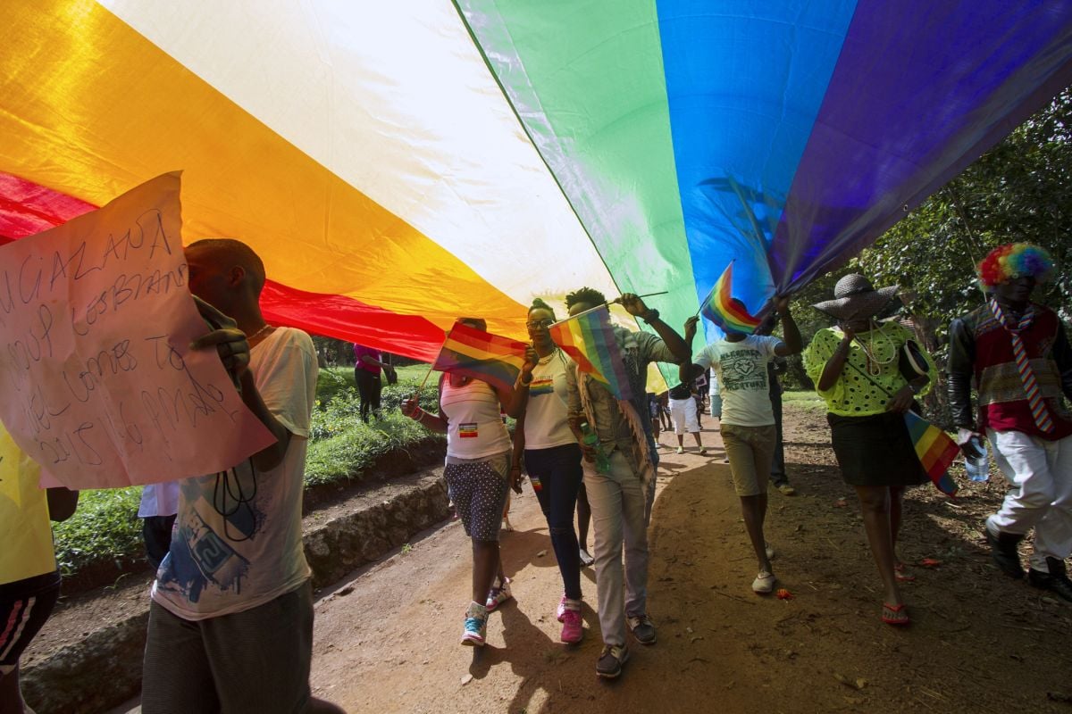 People walk beneath a large stretched out rainbow flag