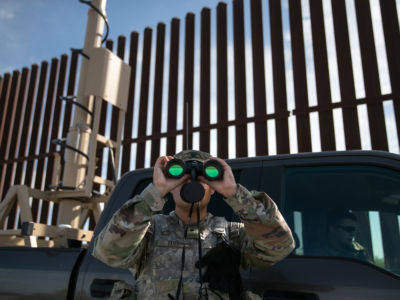 a man in army camoflague looks out with binoculars