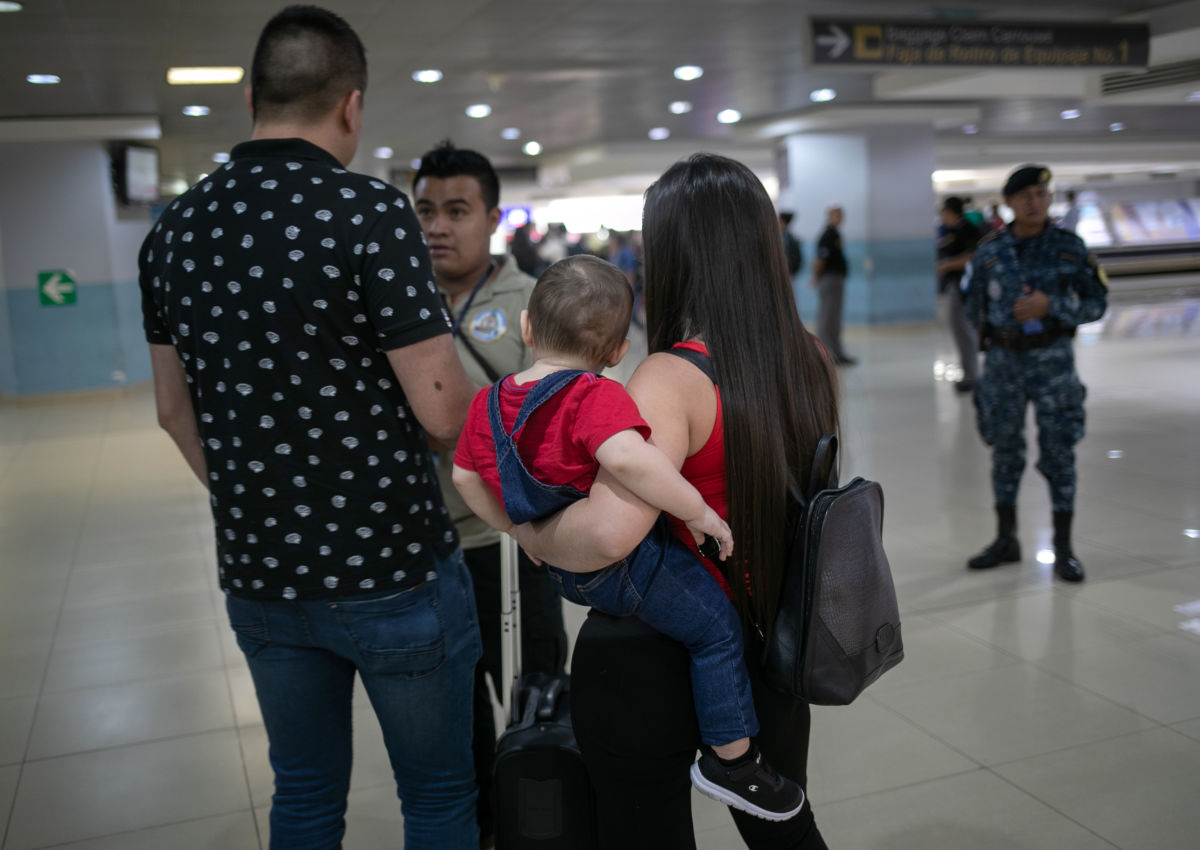 A woman holding a baby and a man speak to another man in uniform while in an airport