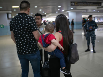 A woman holding a baby and a man speak to another man in uniform while in an airport