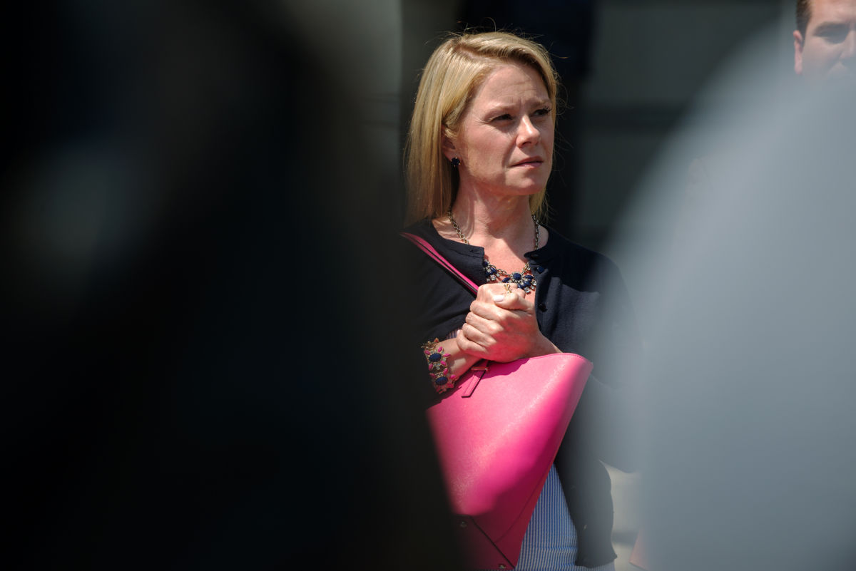 Bridget Kelly stands behind two figures while holding a pink bag