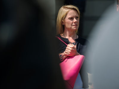 Bridget Kelly stands behind two figures while holding a pink bag