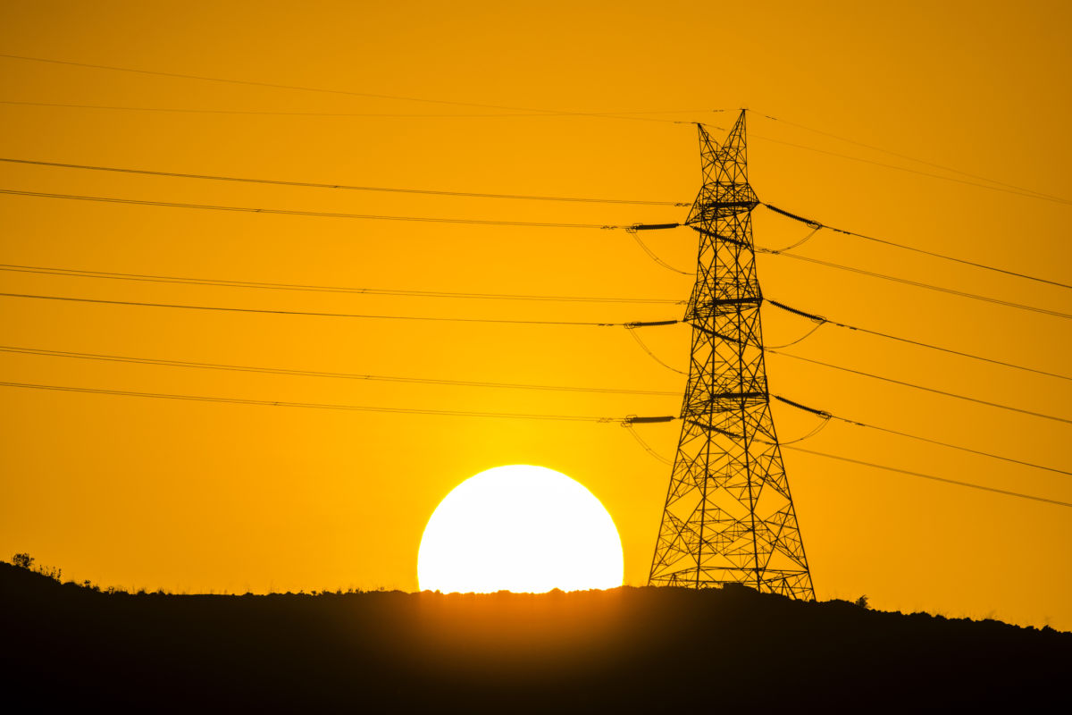 An electrical tower is silhouetted against the setting sun