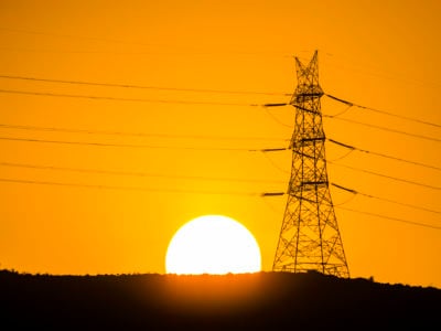 An electrical tower is silhouetted against the setting sun