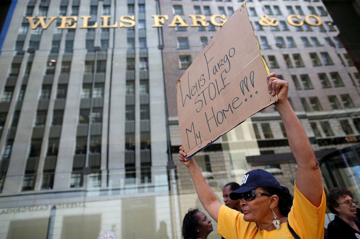 A woman holds a sign reading "WELLS FARGO STOLE MY HOME" during a protest