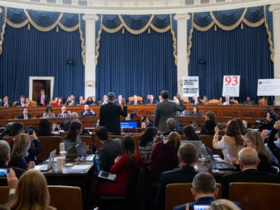 People crowd a room during a hearing where two men raise their right hands to swear an oath