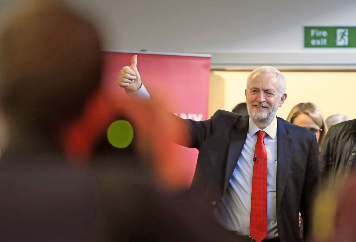 Jeremy Corbyn walks into a room and gives a thumbs up to the crowd