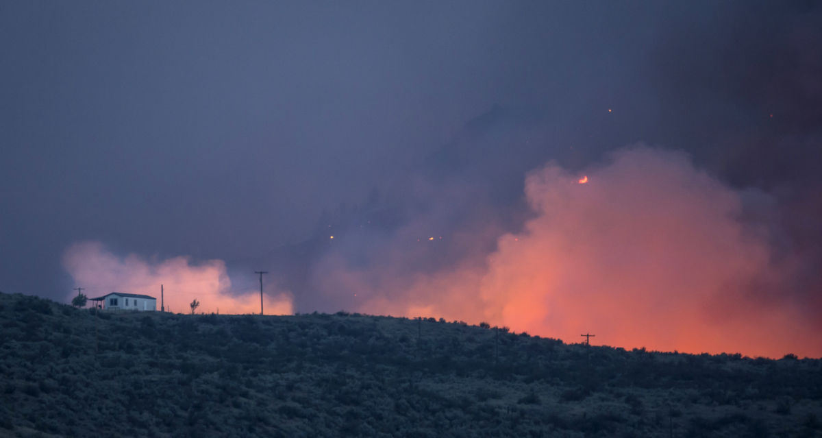 a wildfire lights the horizon where an imperiled house also stands