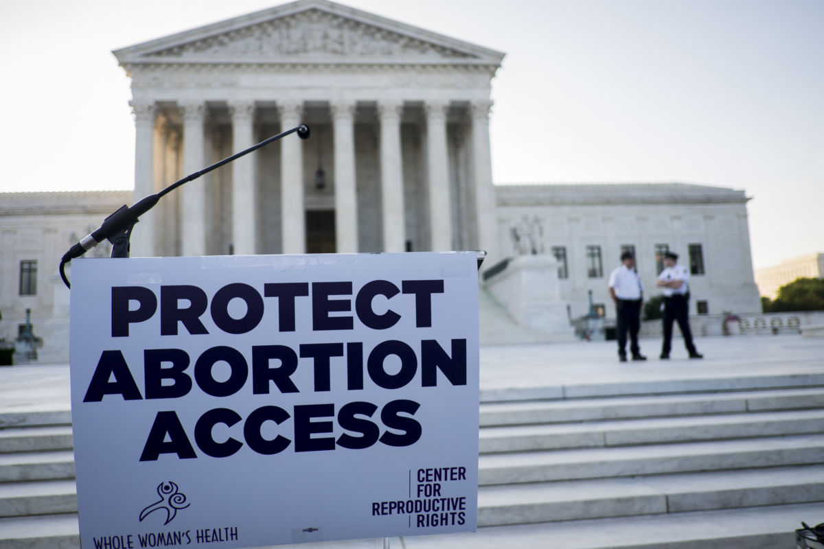 A sign reading "PROTECT ABORTION ACCESS" hangs on a podium in front of the supreme court building