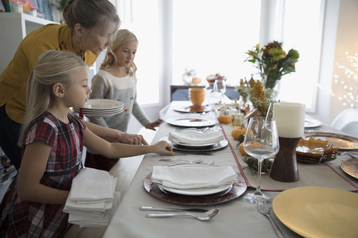 A mother and her young daughters set a Thanksgiving table
